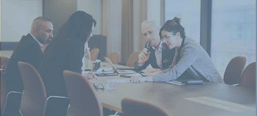 A group of people are having discussion in a conference room at a long desk.