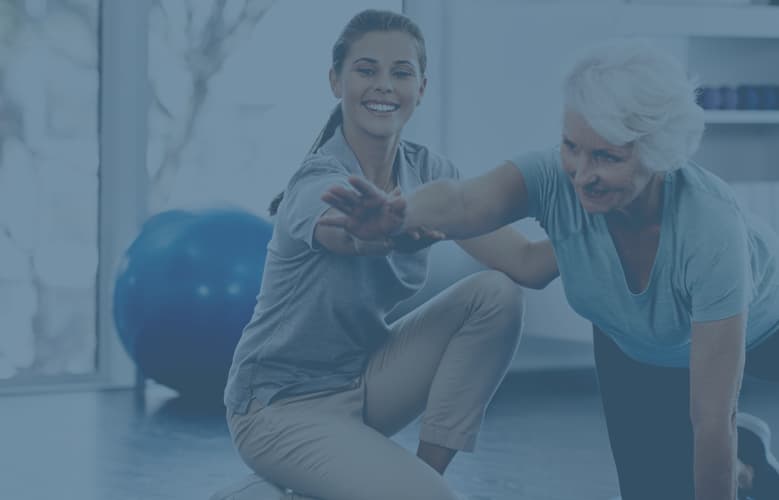 A yoga instructor at a hospital is helping an elderly woman perform a yoga stretch.