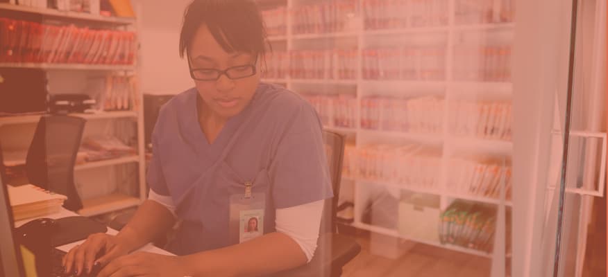 A female doctor in scrubs is doing administrative work in a clinic.