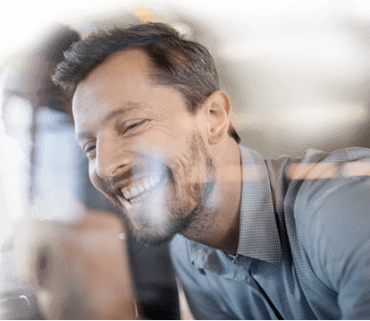 A close-up of a man’s laughing face with a woman in the background.