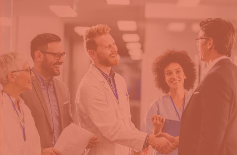 A male doctor surrounded by a group of other smiling doctors is shaking hands with a business man.