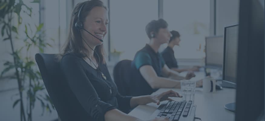 A line of people working at a call center are happily taking calls.