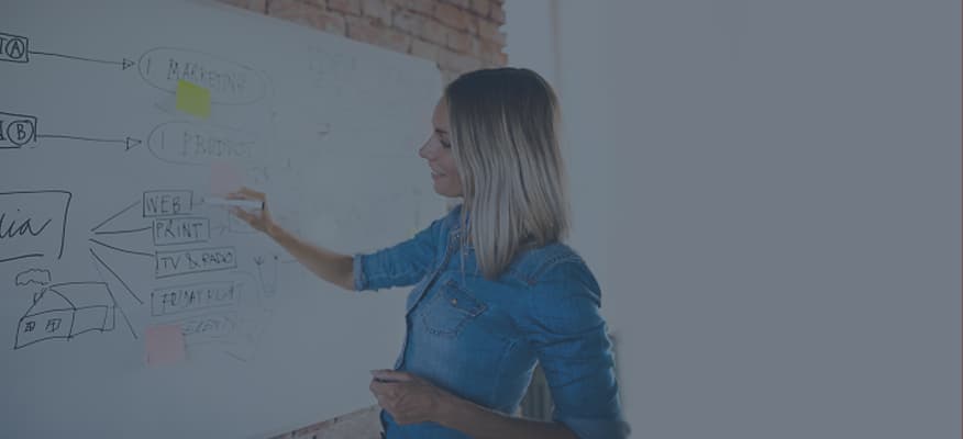 A woman is writing notes on a white board in an office setting.