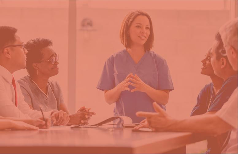A female doctor in scrubs is holding a meeting with her fellow doctors sitting around a table.