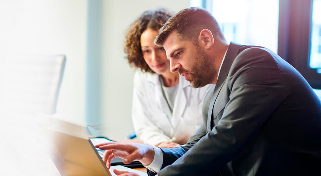A business man is showing a female doctor data on a computer screen.